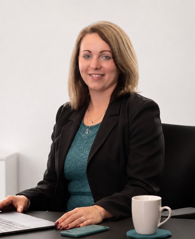 Portrét Lucie Lacinové u pracovního stolu, v černém saku a petrolejových šatech